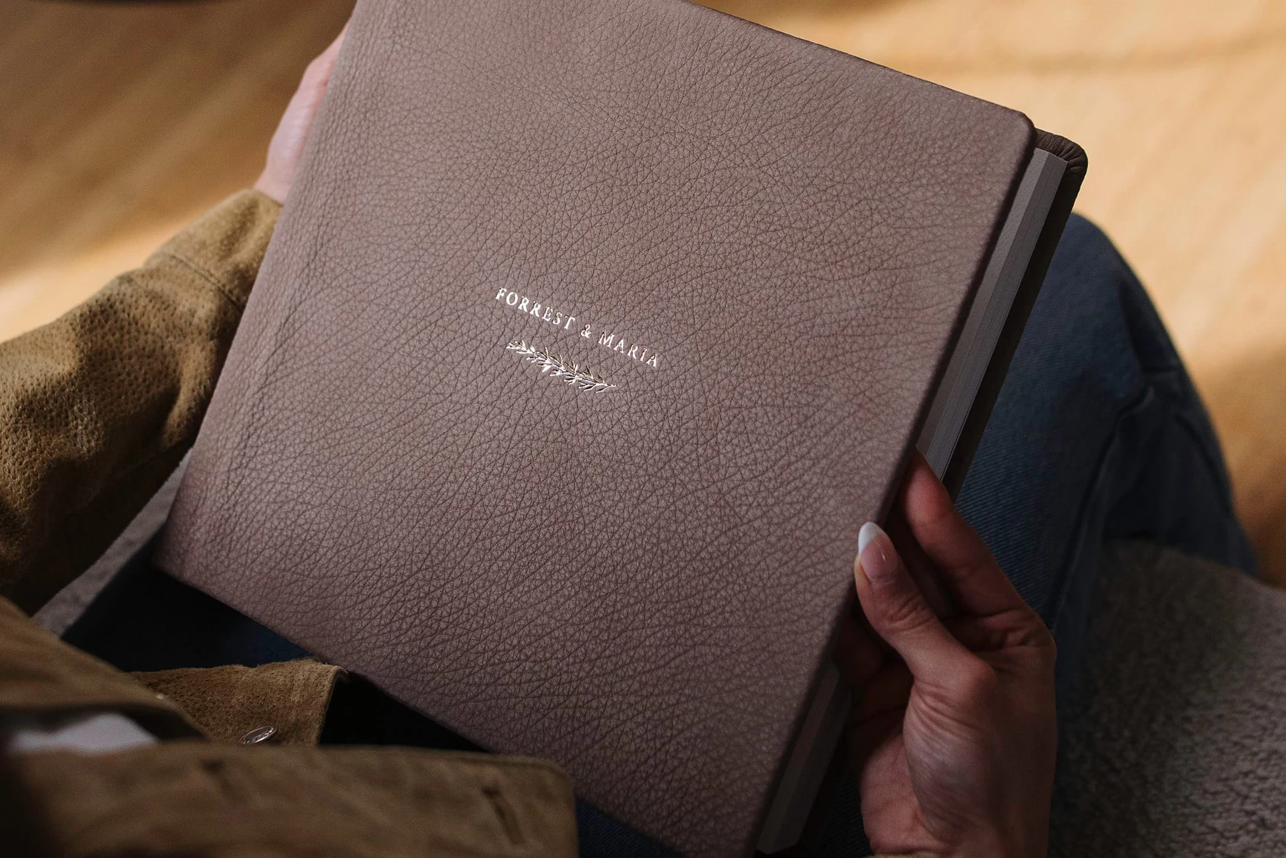 A personalized leather album held in a lap, showing its natural grain
