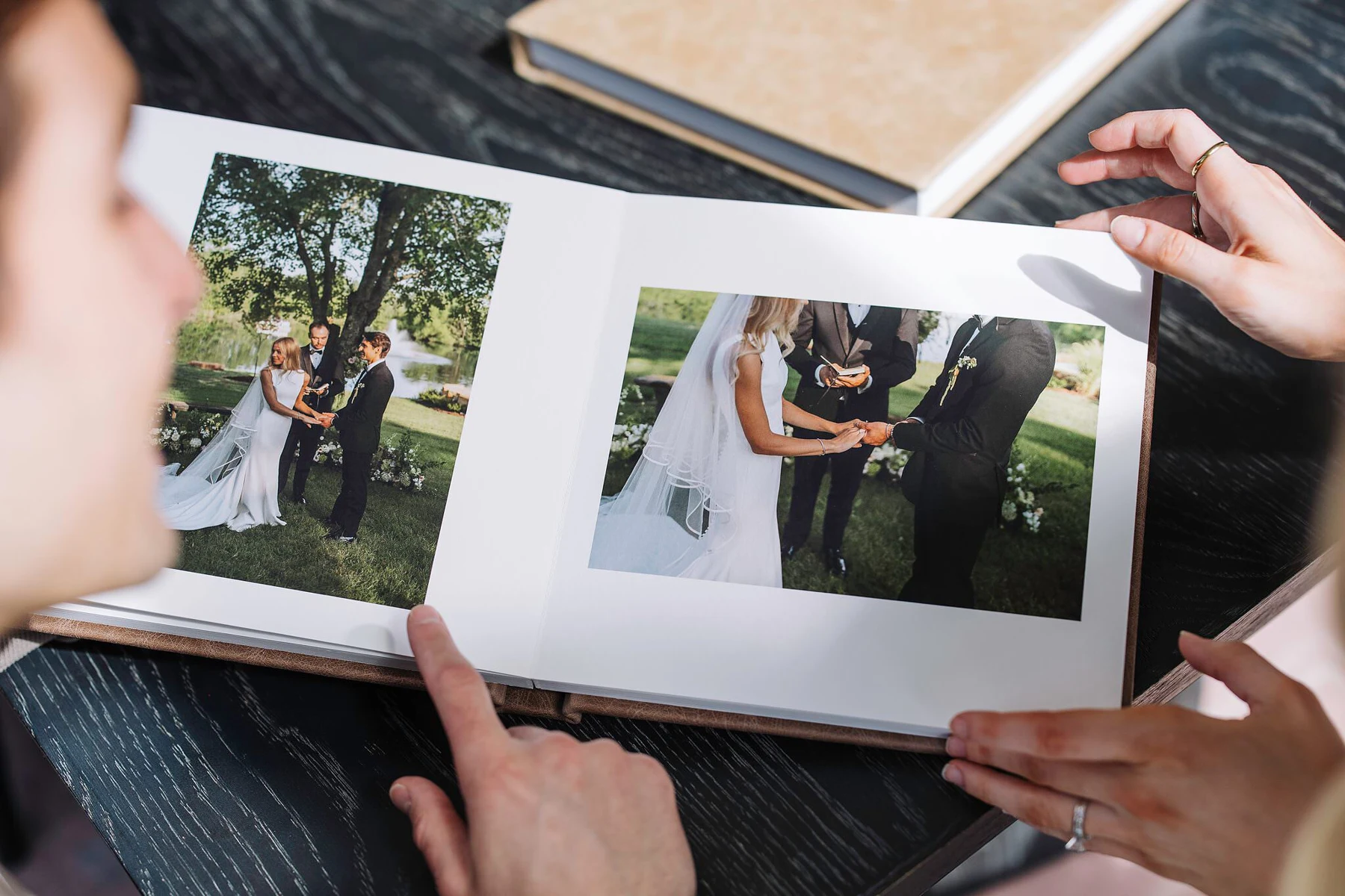 Hands holding an open wedding album with photographs of a couple exchanging vows
