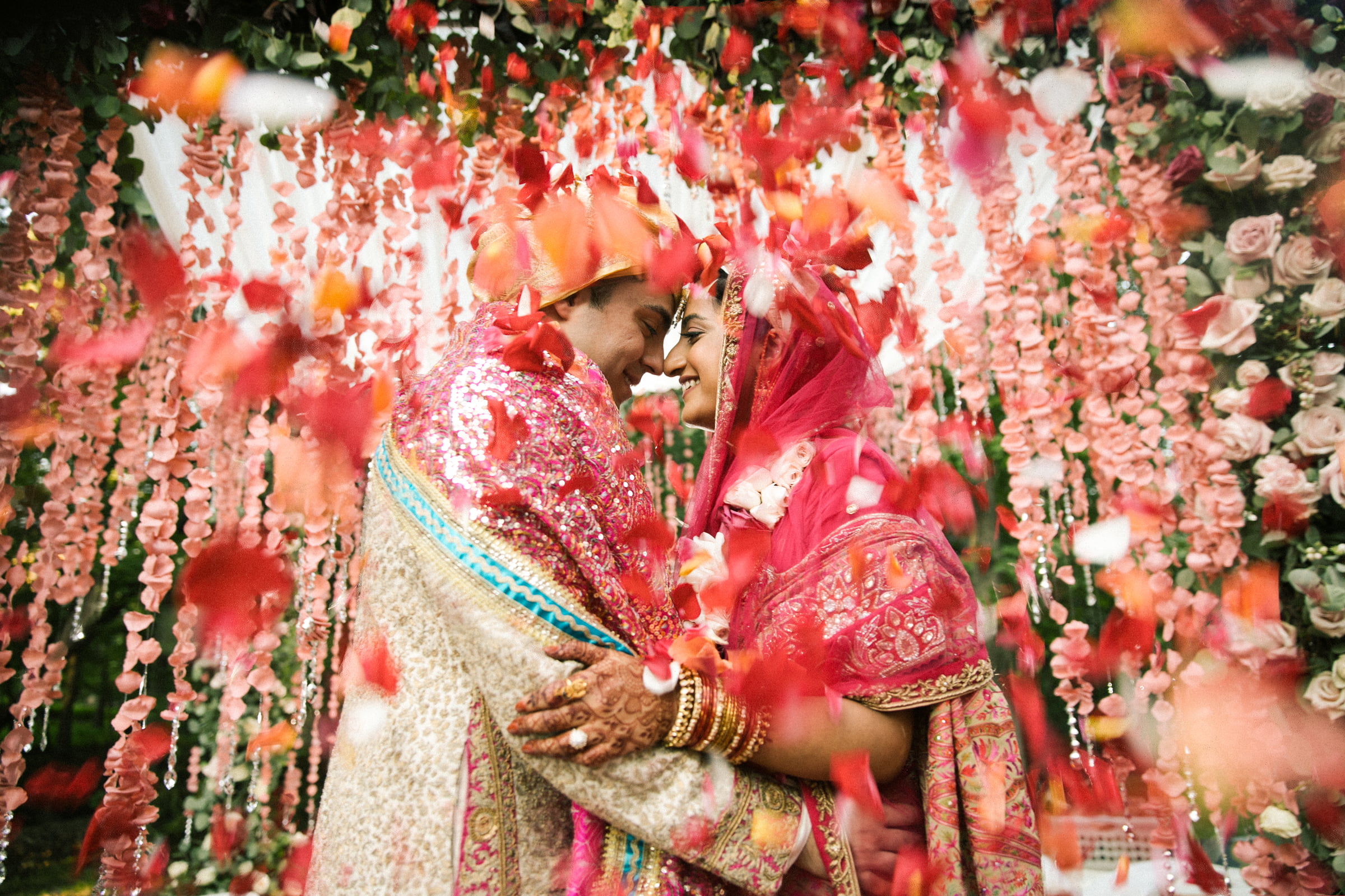 A joyful wedding kiss surrounded by garlands and falling red petals