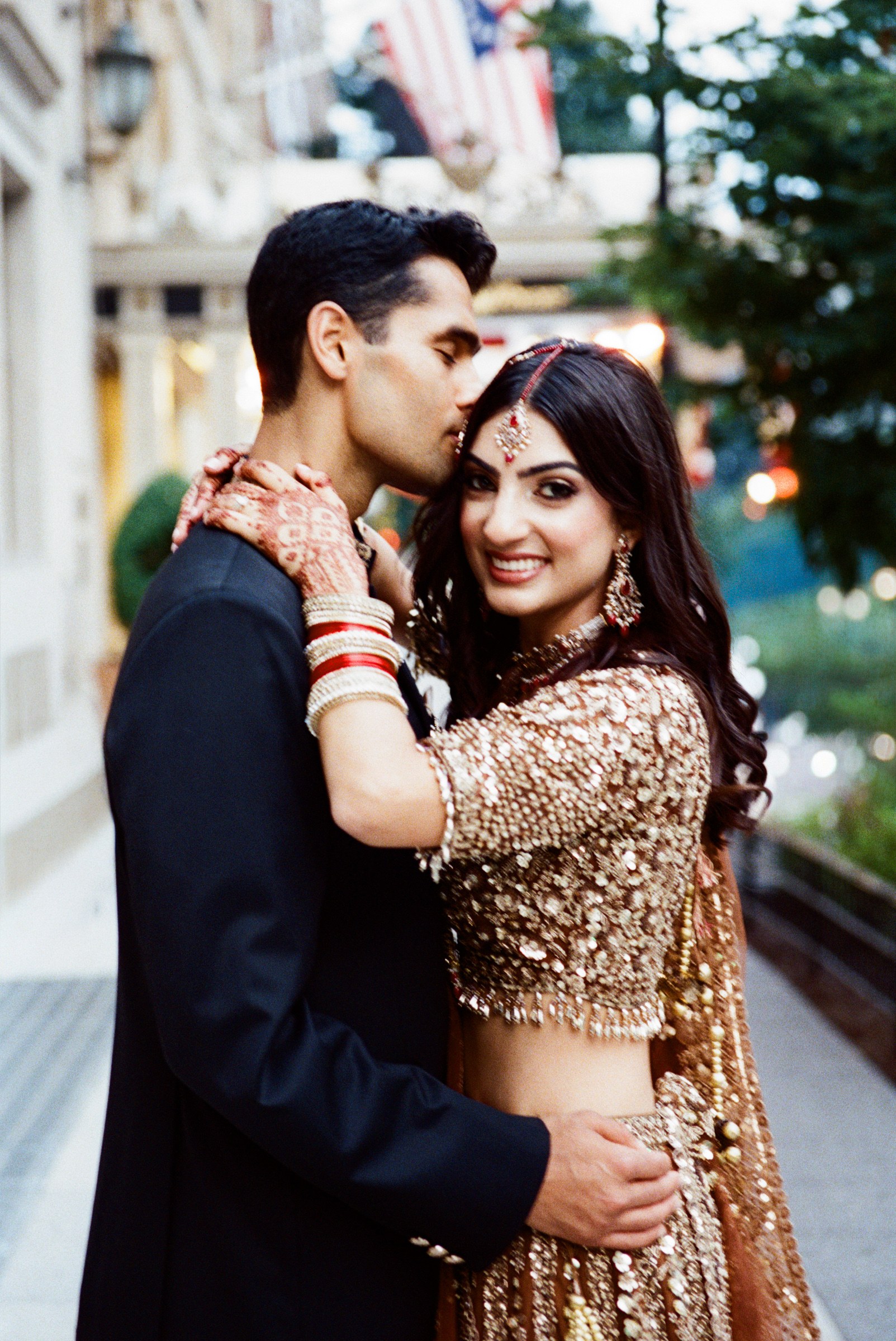 A groom kissing the bride’s forehead on a city street, photographed on 35mm film